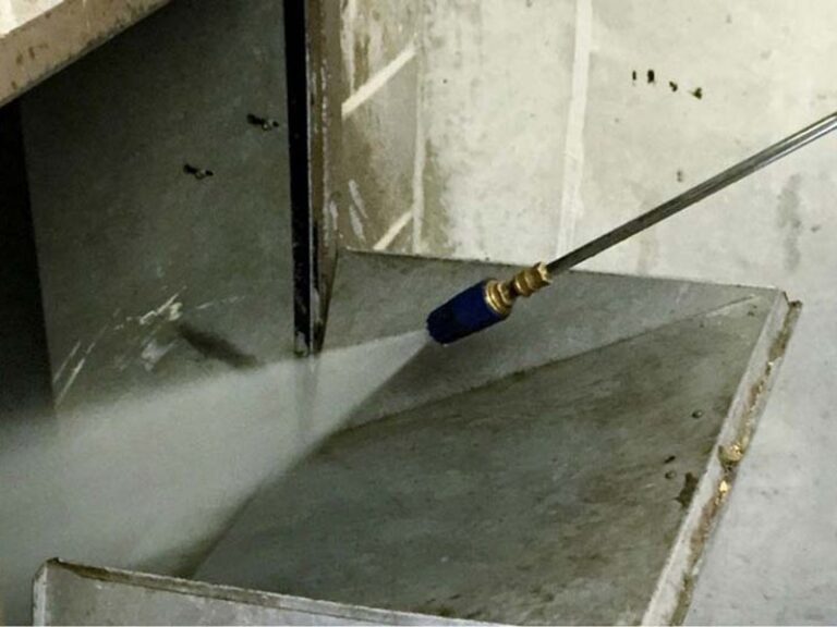 Picture of a pressure washer straying the inside of an apartment building trash chute.